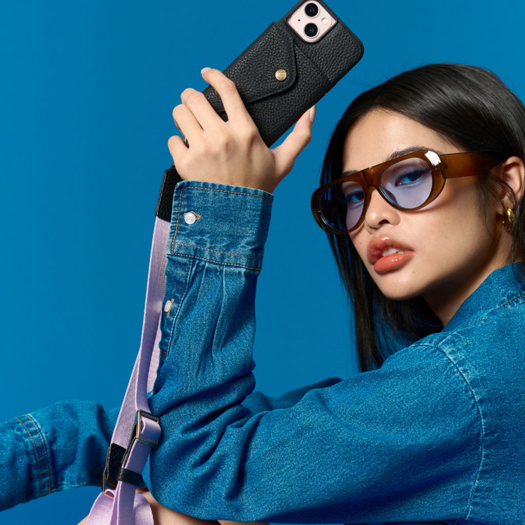 Model wearing the black Bandolier-style leather crossbody phone case, demonstrating its practicality with the adjustable strap comfortably slung over the shoulder.